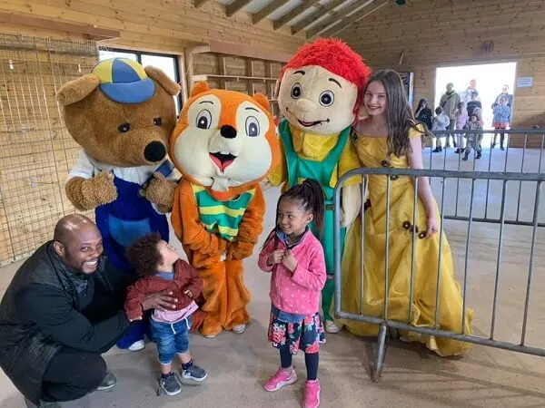 Adult and young children pose with costumed characters inside a farm venue building.