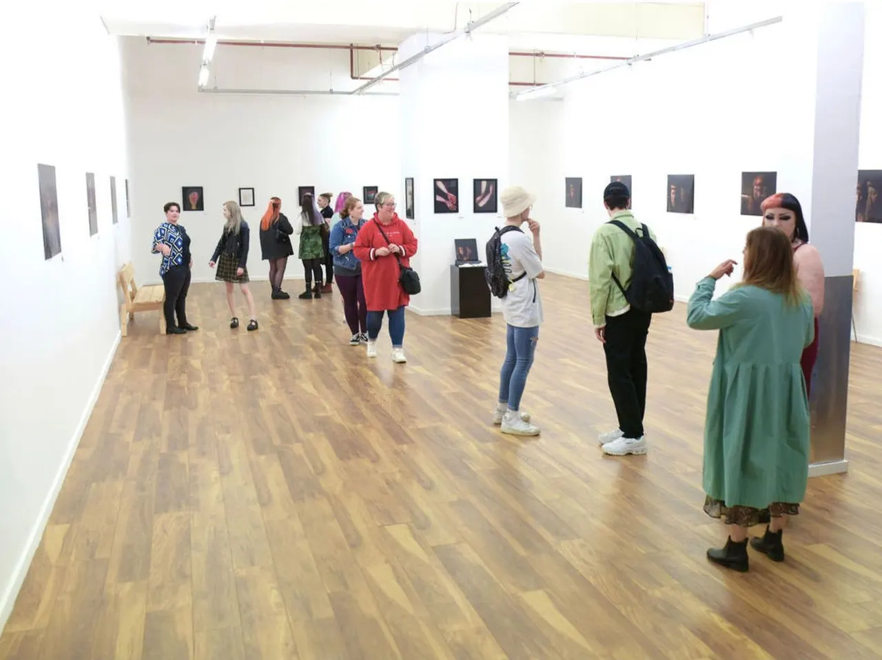 Visitors view portrait photographs displayed on white walls in a bright gallery space with wooden flooring.