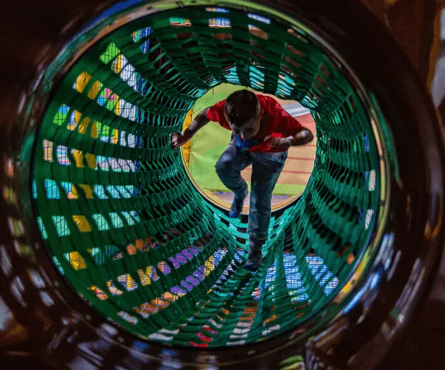 Child crawling through a green tunnel at an indoor play facility.
