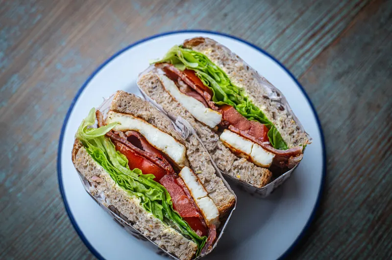 Two wholemeal sandwiches filled with bacon, lettuce, tomato and cheese on a white plate with blue rim.