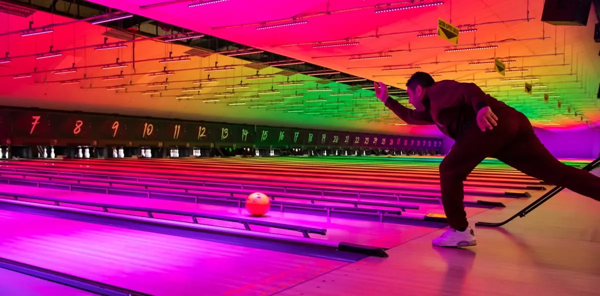Person bowling on a neon-lit lane with colourful overhead lighting and numbered pins visible.
