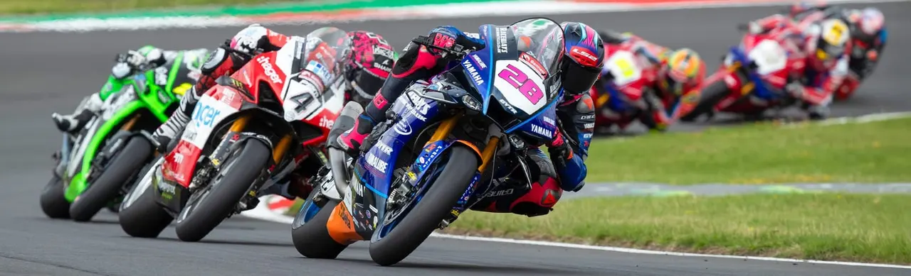 Pack of motorcycle racers leaning into a turn during a competitive race on an asphalt circuit.