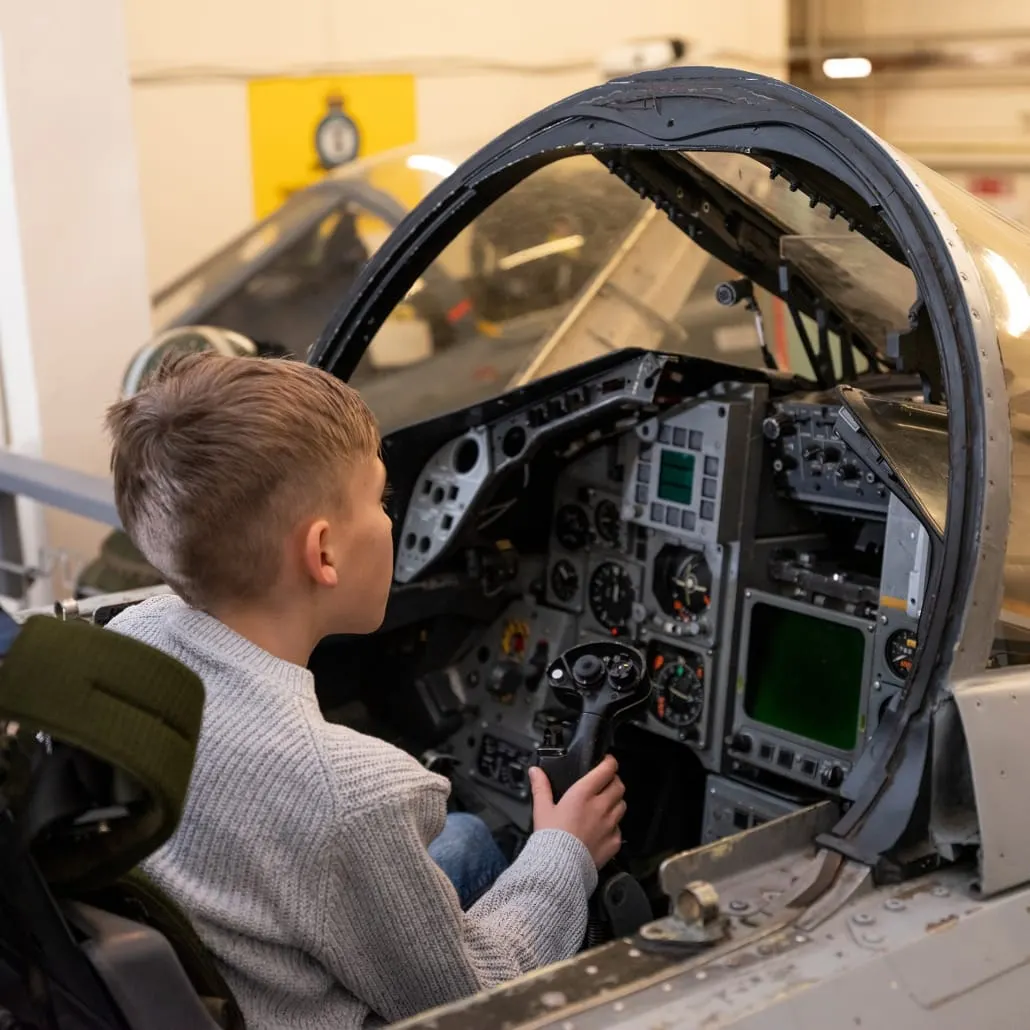 Child sitting in aircraft cockpit simulator, operating controls and looking at instrument panel.