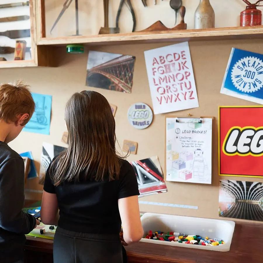 Two children viewing displays and building blocks at a hands-on museum exhibit with artwork and educational materials pinned to walls.