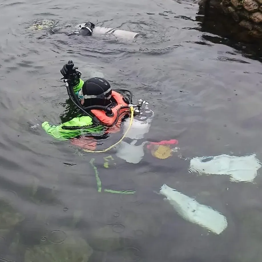 A scuba diver in bright orange and neon gear descends underwater whilst another diver surfaces in the background during a training dive.