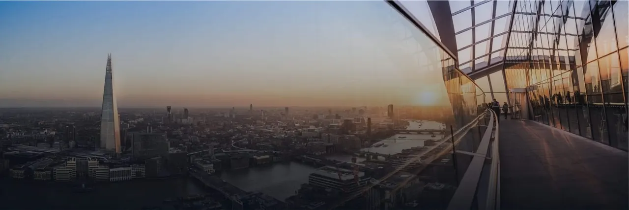 People on an open-air observation deck overlooking London's skyline at sunset, with the Shard and Thames visible.