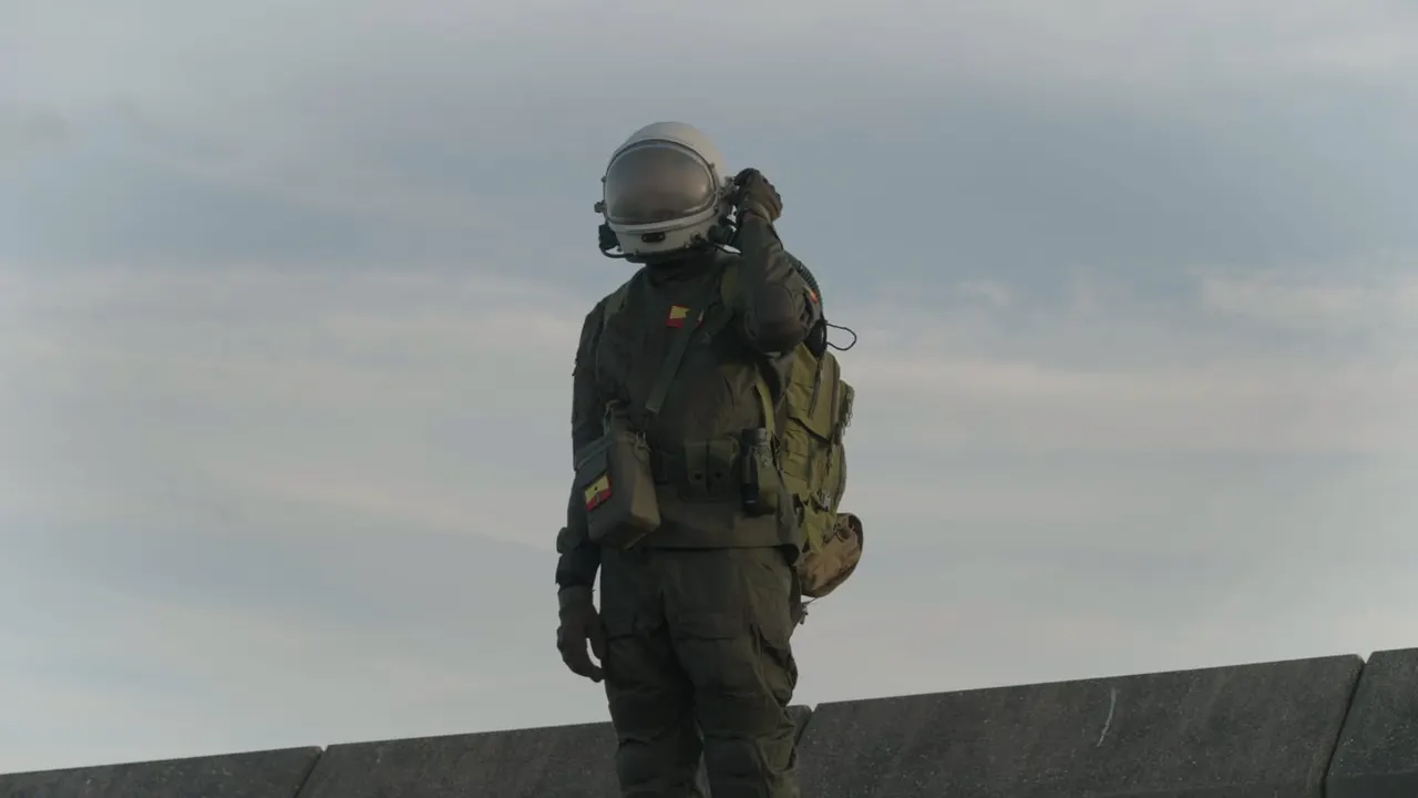 Person in full astronaut suit and helmet standing on a concrete structure against a cloudy sky.