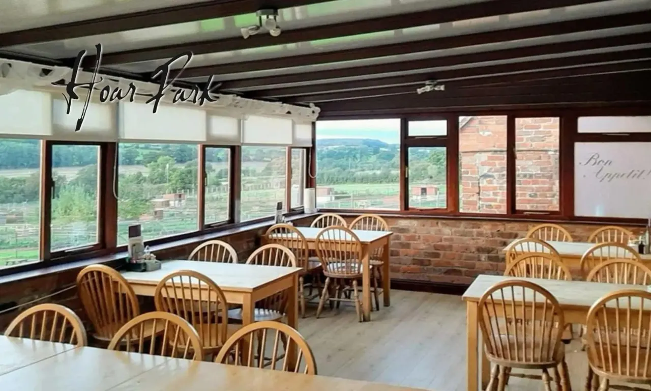 Dining room with wooden tables and chairs overlooking countryside fields and hills through large windows.