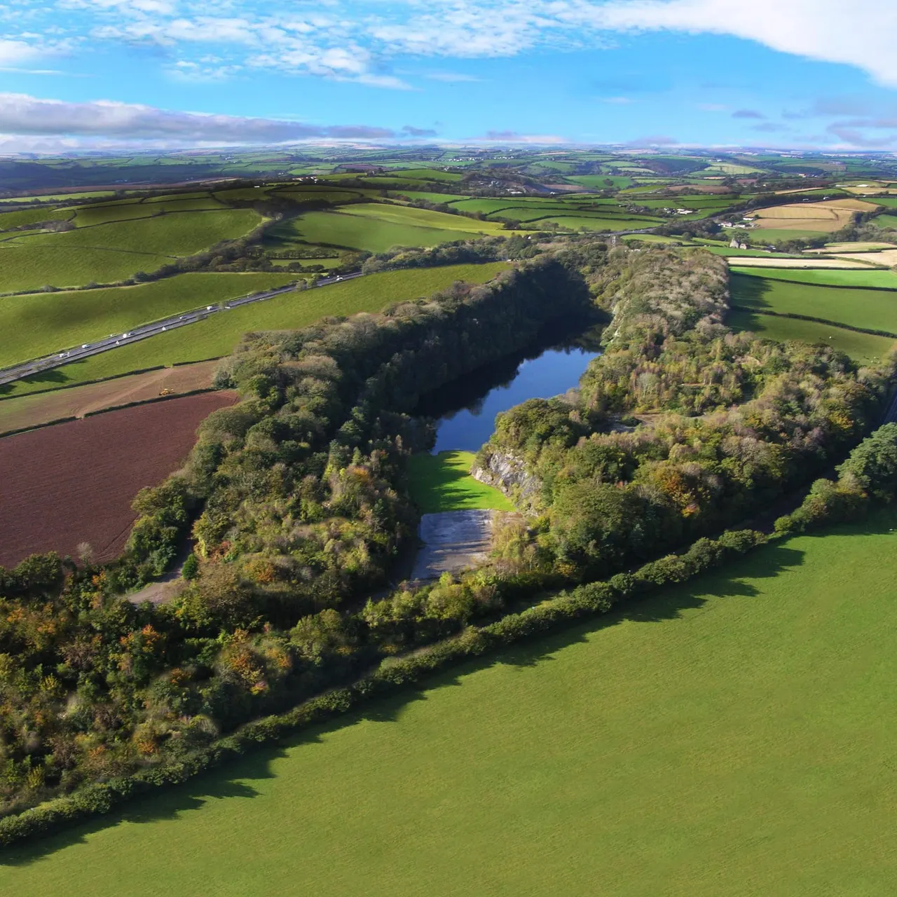 Aerial view of a river flowing through a wooded gorge surrounded by green farmland and fields.