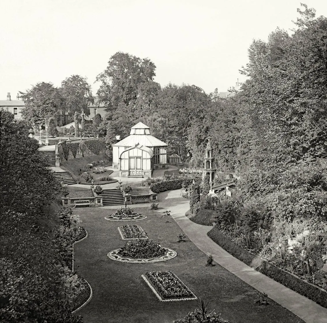 Formal Victorian garden with octagonal glasshouse, hedged beds, pathways and tall trees surrounding manicured grounds.