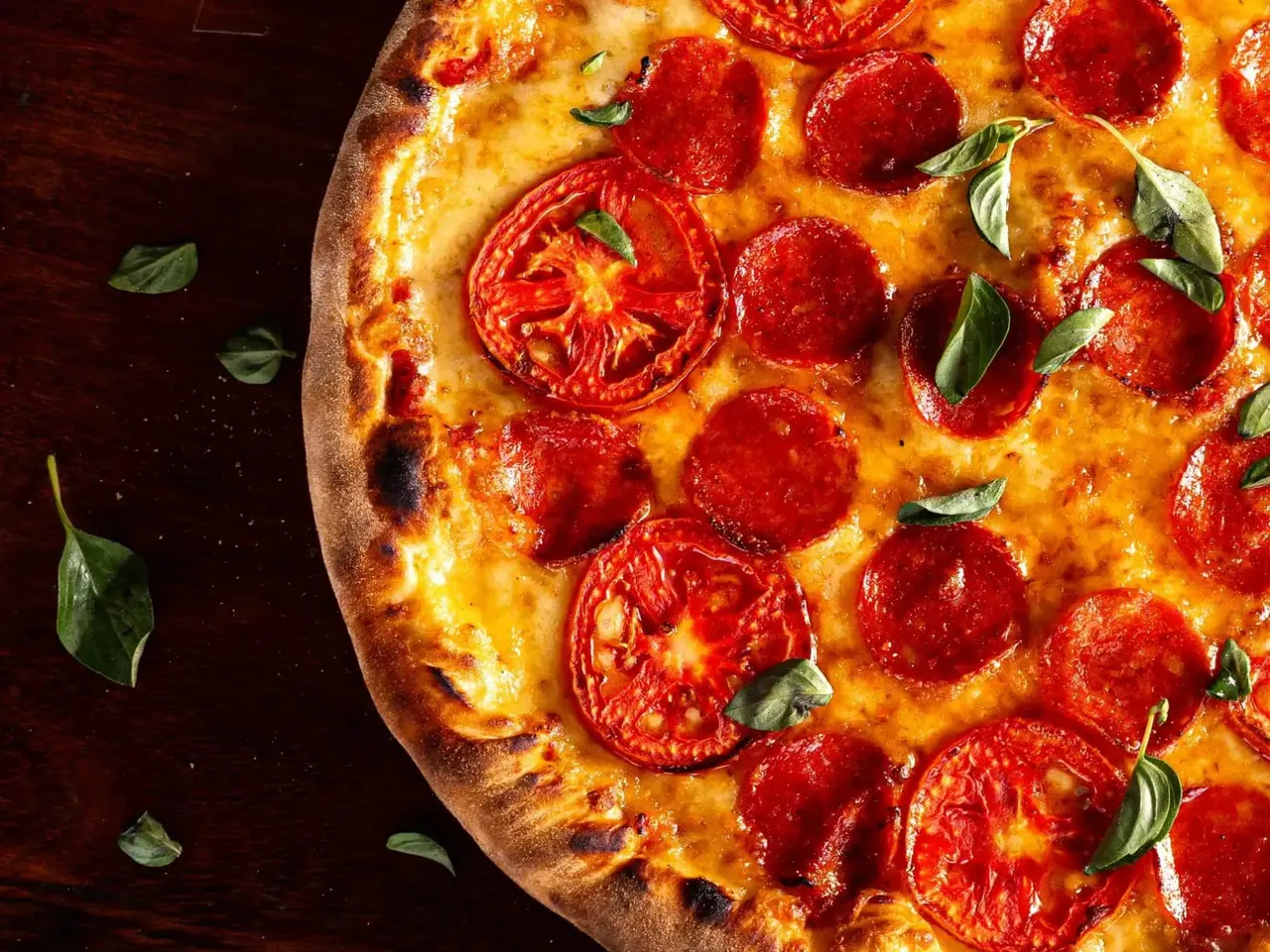 Freshly baked pizza topped with melted cheese, tomato slices and basil leaves on a dark surface.