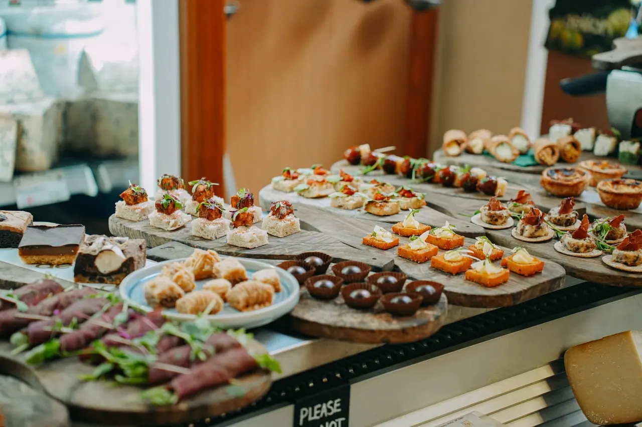 Catering display with assorted savoury canapés, pastries, chocolate confections and cured meats arranged on wooden boards and plates.