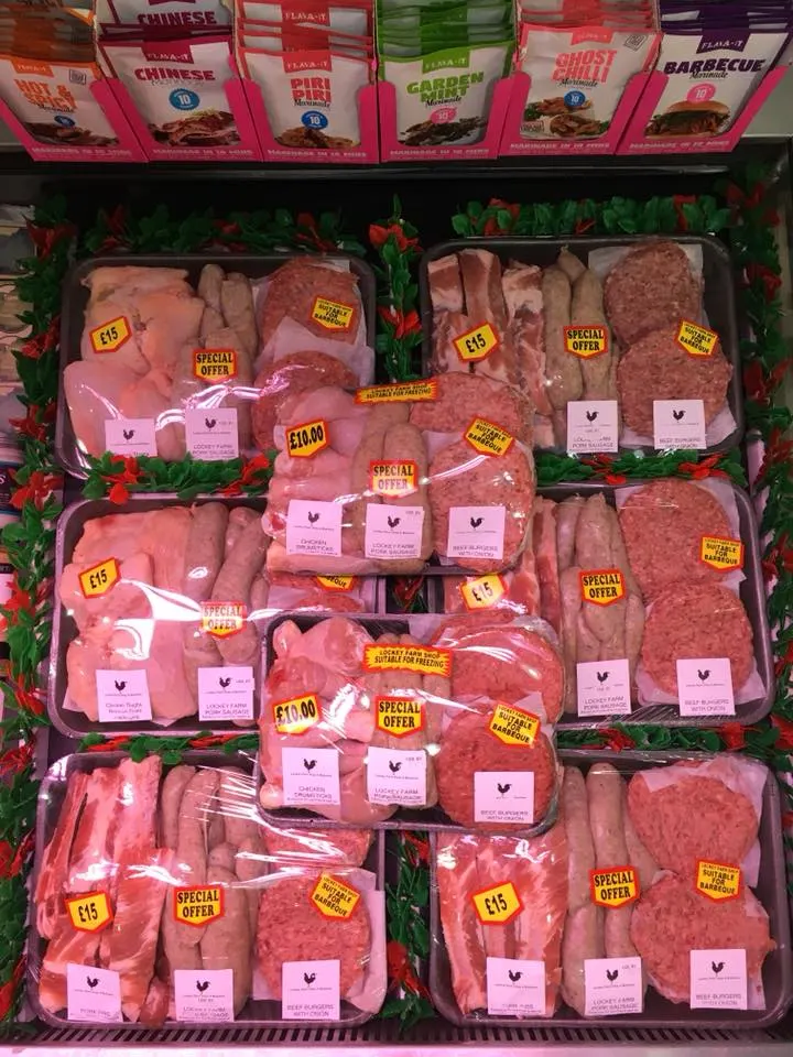 Butcher's display case with packaged fresh and processed meat cuts with price labels and special offer stickers.