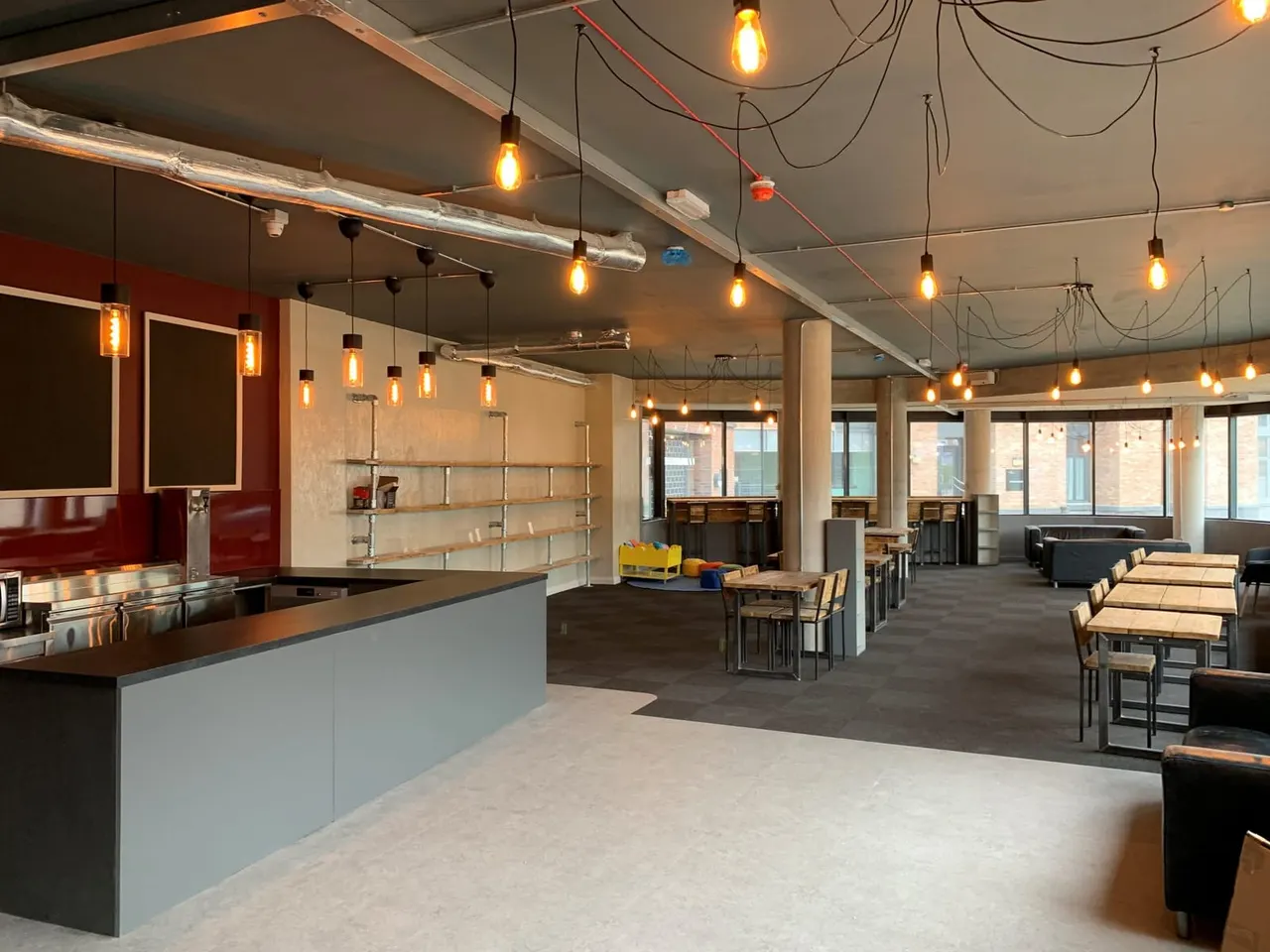 Modern café interior with service counter, dining tables and chairs, and warm pendant lighting throughout the space.