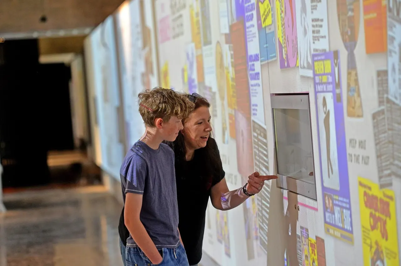 An adult and child viewing an interactive display panel at a museum exhibition about local history.