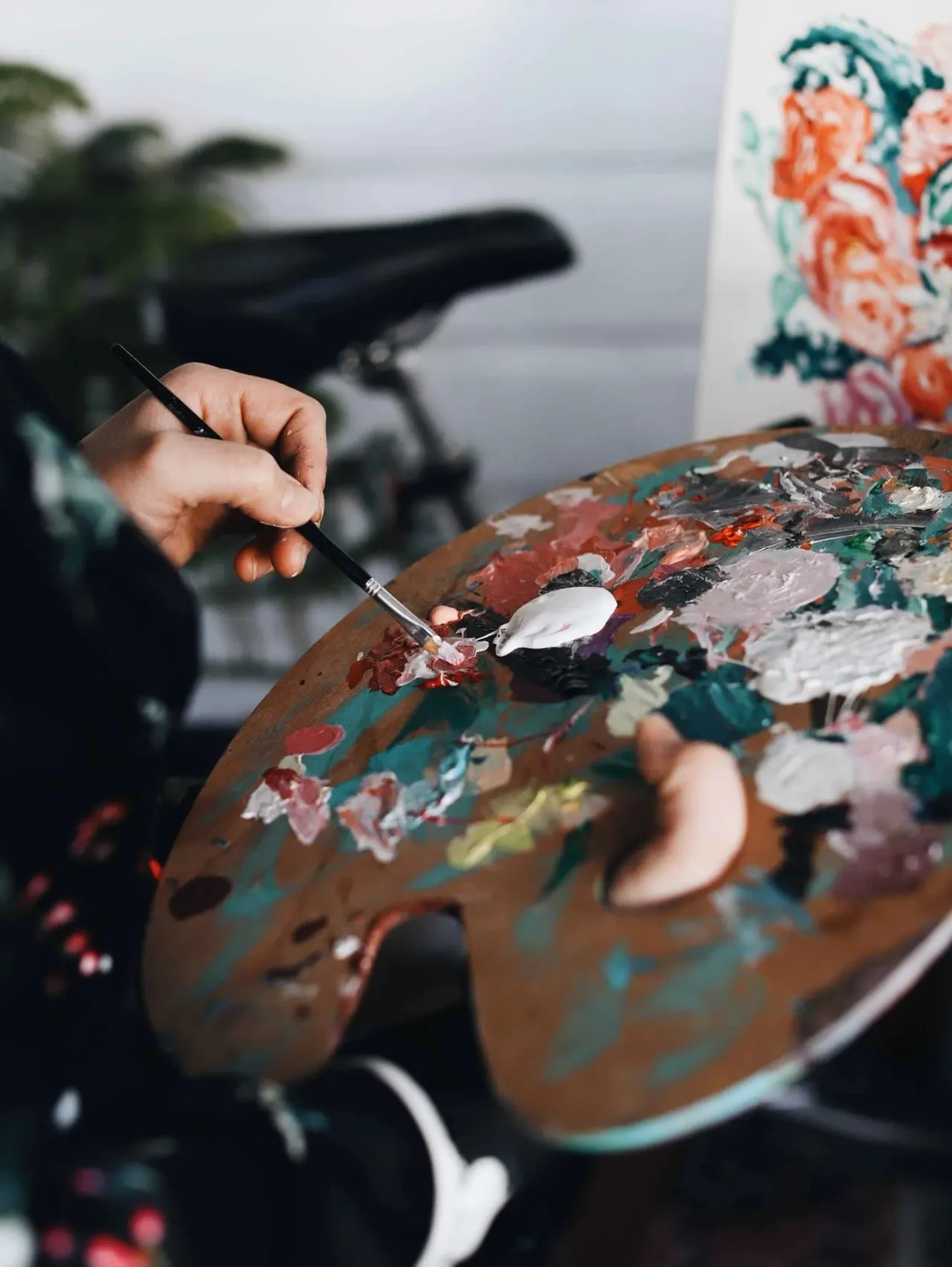 Artist painting on a palette with a brush overlooking water and a telescope.