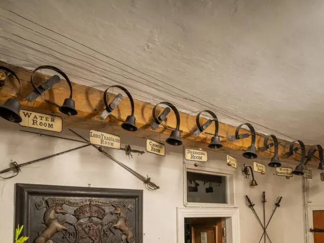 Row of vintage barn lamps with black shades mounted on whitewashed ceiling above doorways and decorative items.