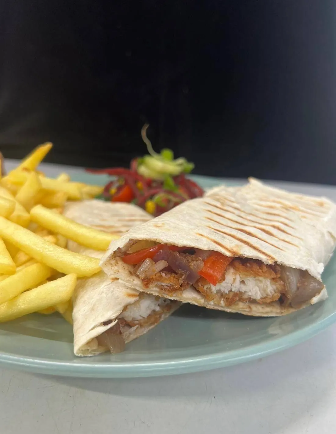 A plate with a filled pita sandwich, chips and fresh strawberries against a dark background.