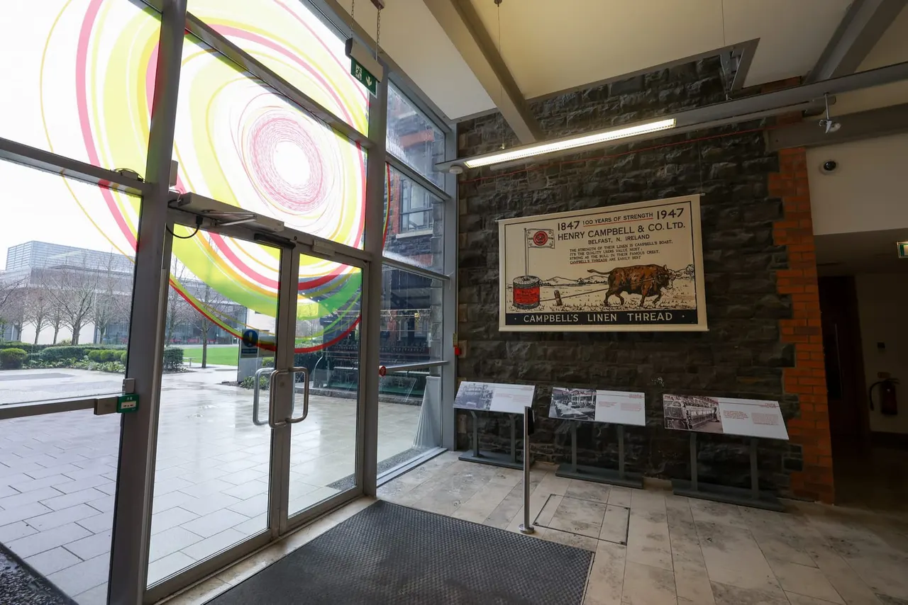 Museum entrance with neon spiral art installation and vintage Campbell's Linen Thread advertising poster on stone wall.