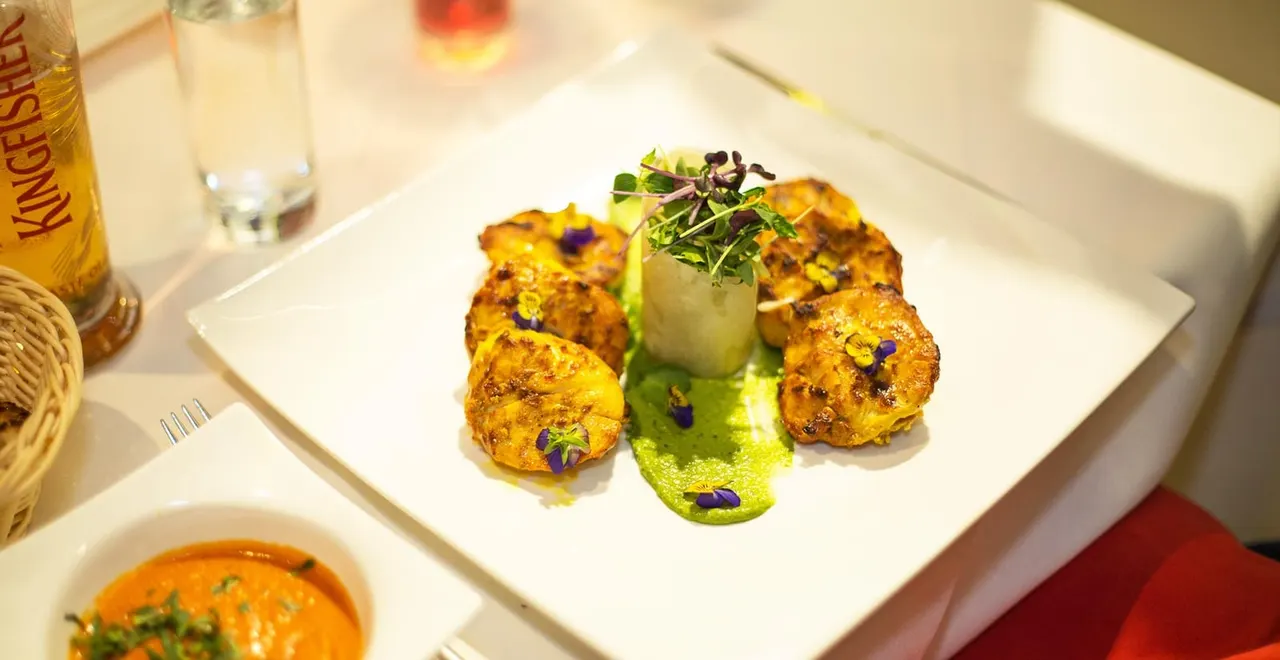 Plated dish of golden-seared scallops with green sauce, microgreens and purple flowers on white plate.