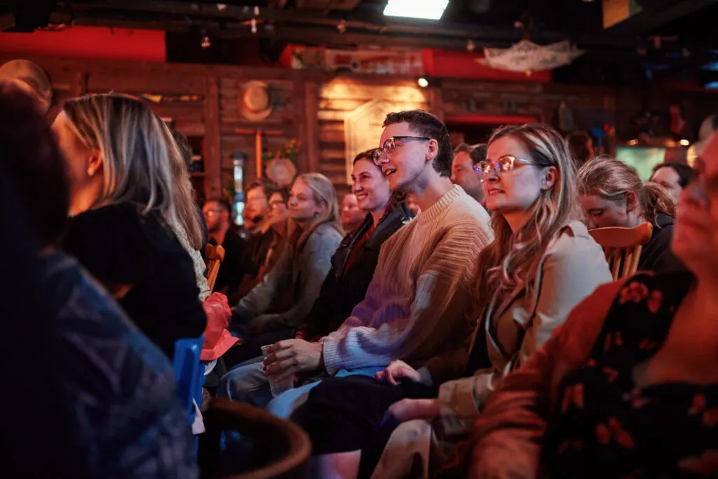 A crowd of people sitting together in a warmly lit indoor venue, watching an event or performance.