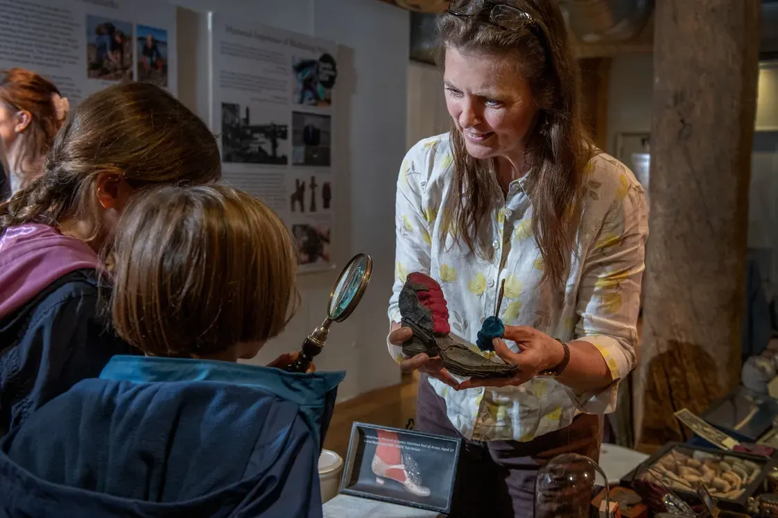 A museum educator shows children an artefact and magnifying glass during a hands-on learning activity.