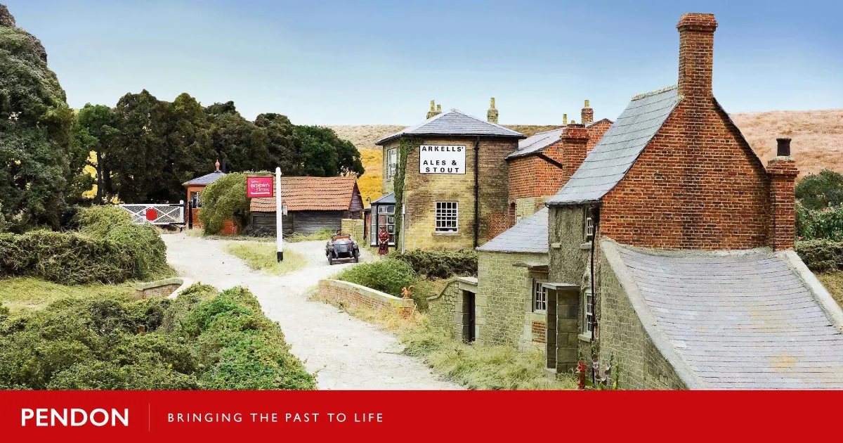Historic village street scene with brick buildings, a sign for Arkells Ales & Stout, and rolling countryside under clear sky.