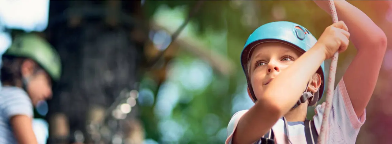 Young child wearing a blue helmet gripping a rope during an outdoor climbing activity.