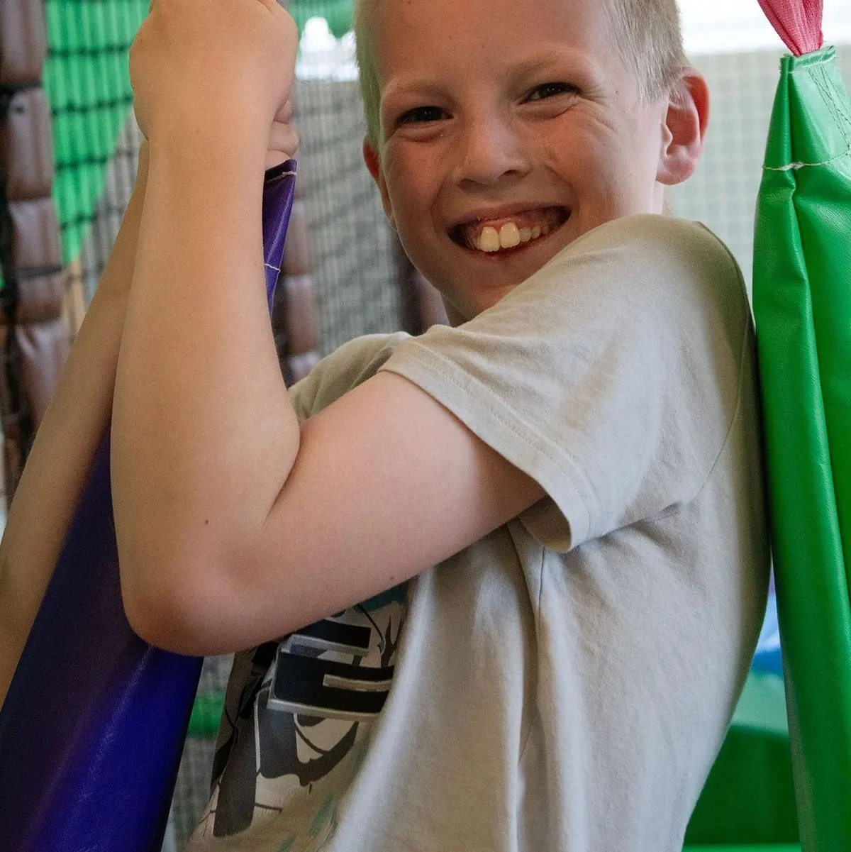 Young boy smiling at camera while flexing his arm inside an indoor soft play facility.
