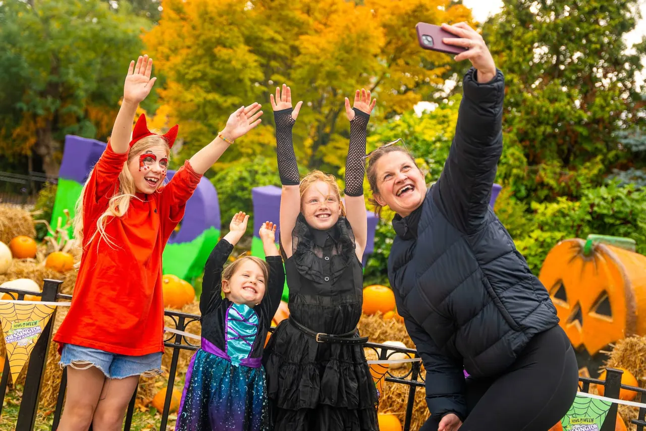 An adult and children in Halloween costumes celebrating outdoors among autumn decorations and pumpkins.