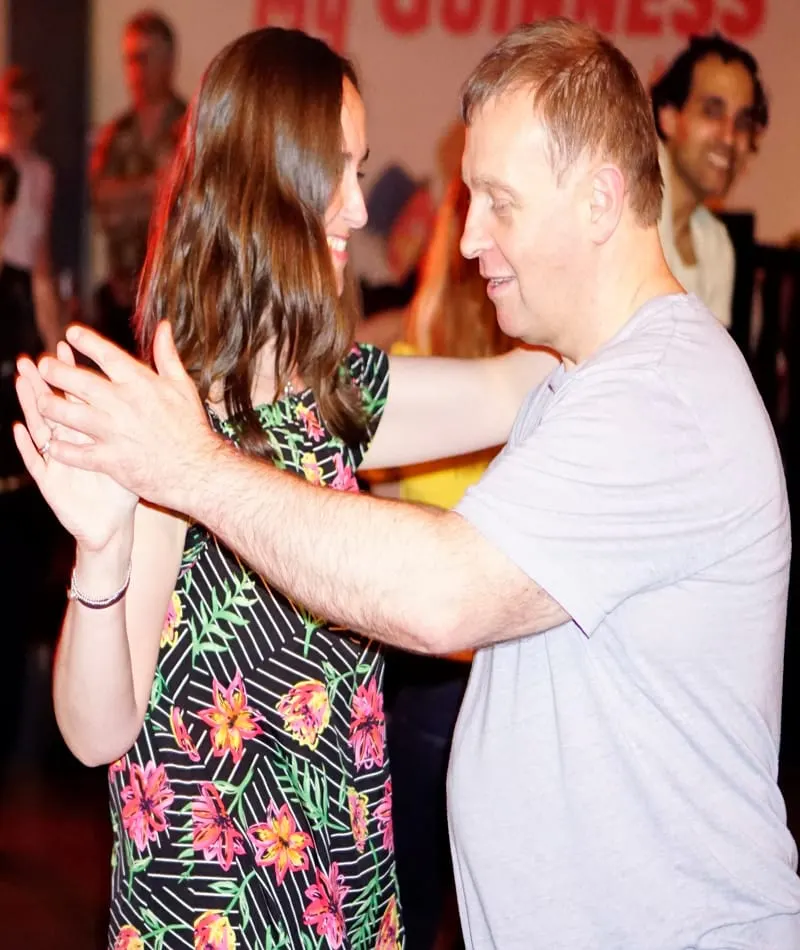 Two people dancing together at a social dance event with others visible in the background.