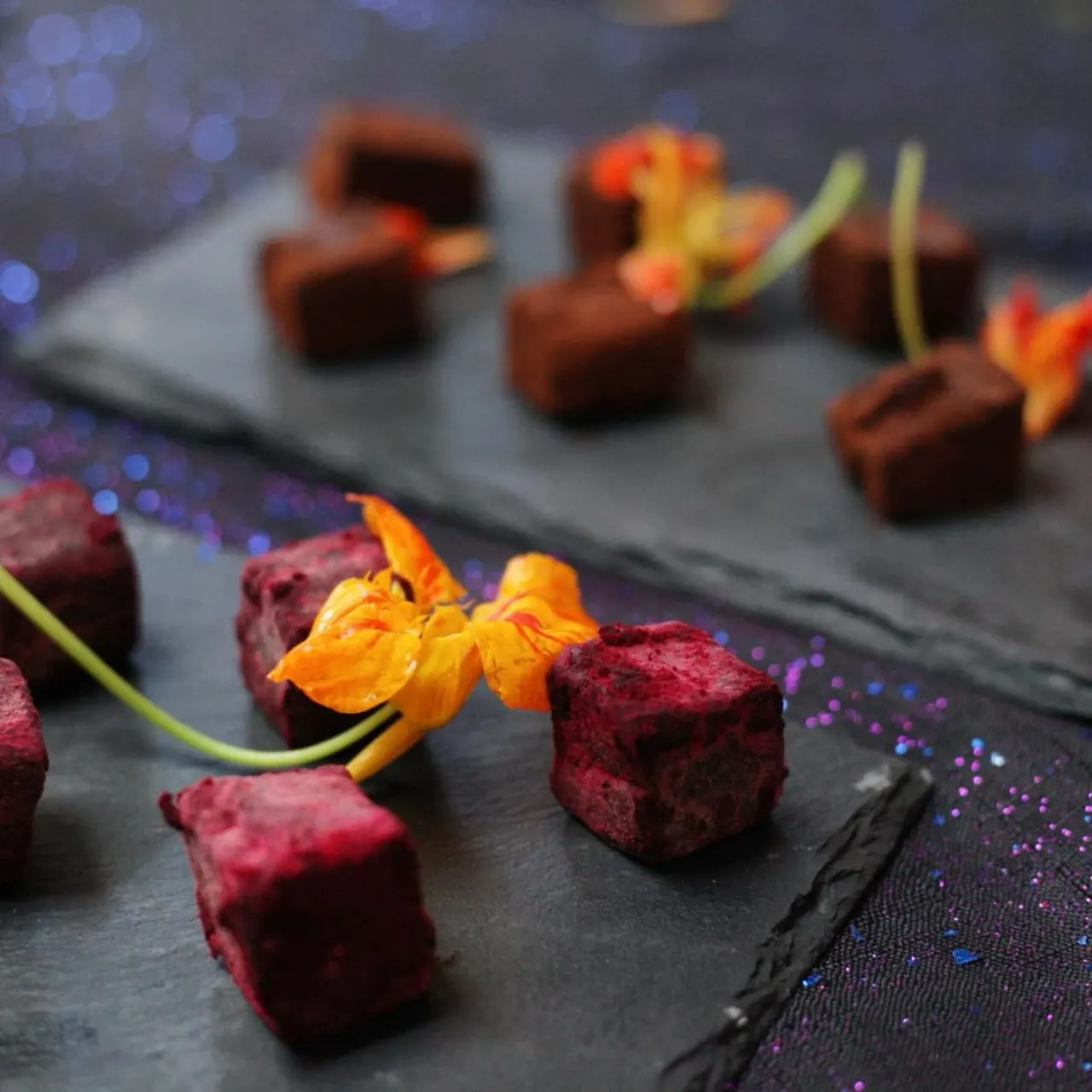 Plated dessert with red and chocolate truffles garnished with orange nasturtium flowers and green stems.