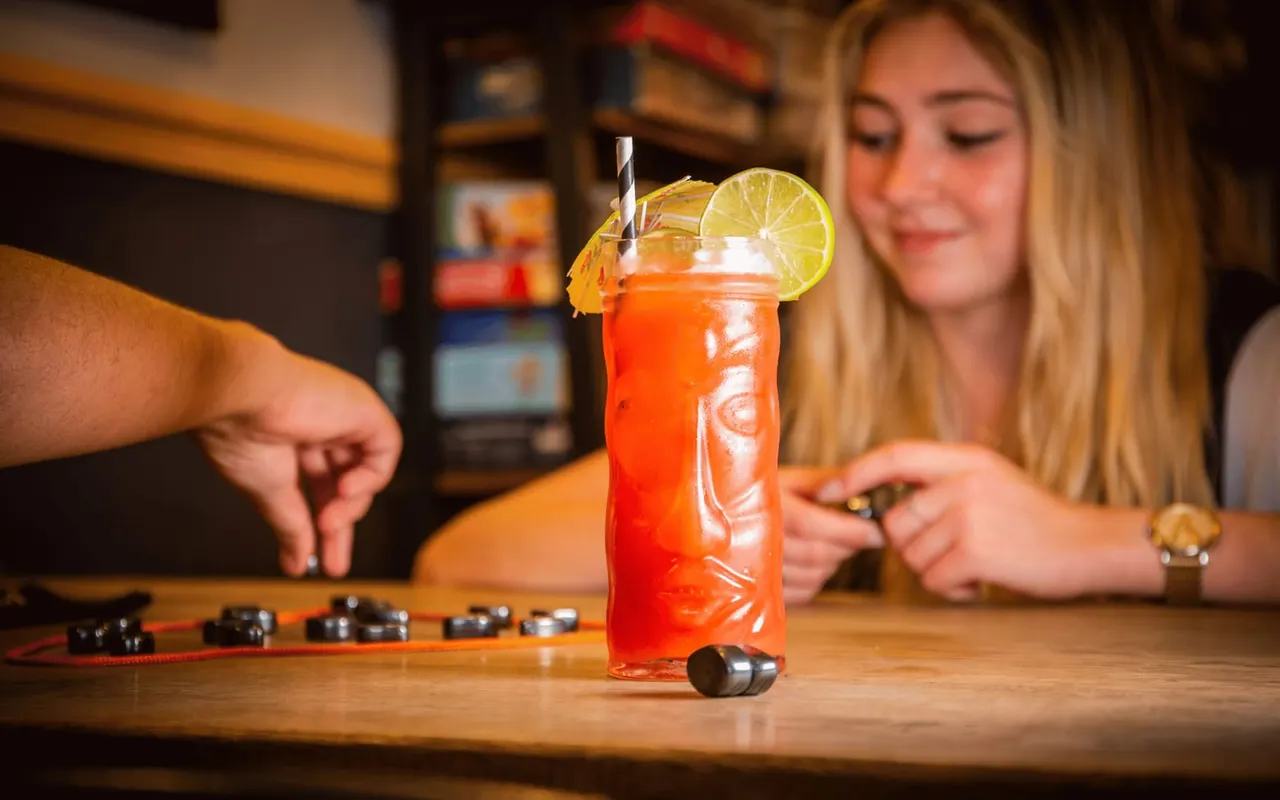 A woman at a bar counter enjoys a bright red cocktail garnished with a lime wheel and striped straw.