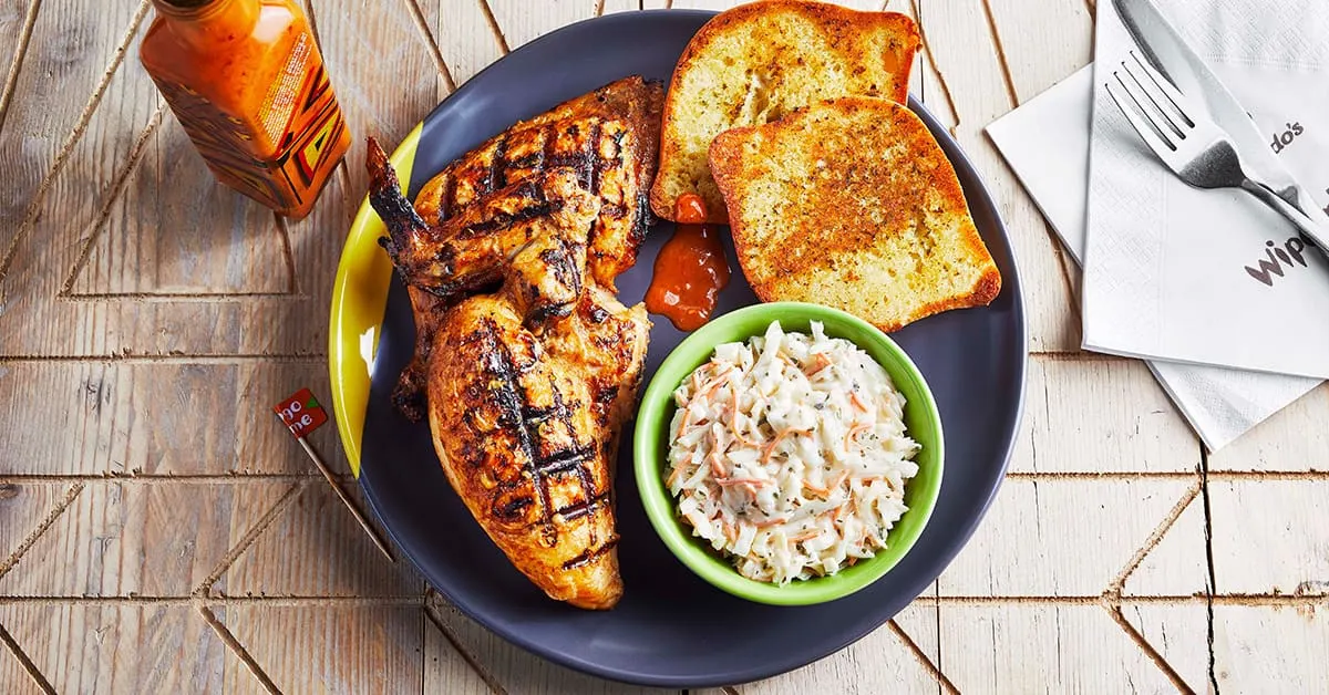 Grilled chicken breast with char marks, garlic bread, coleslaw and sauce on a dark plate.