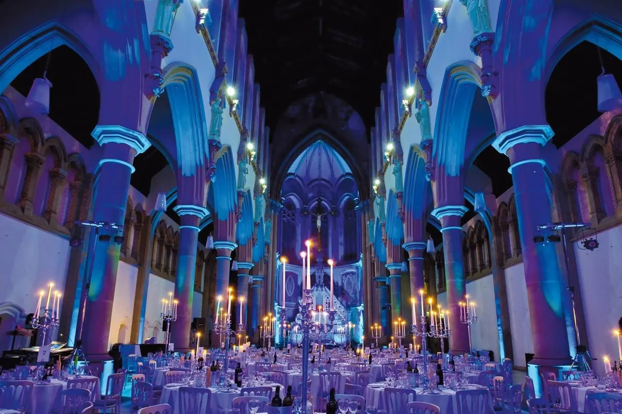 Gothic cathedral interior with blue and purple lighting, set with numerous round dining tables for a large formal event.