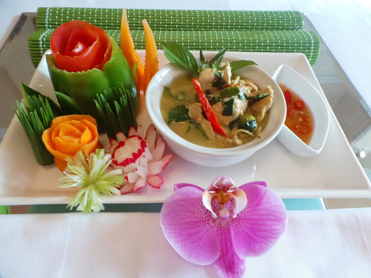 Thai curry dish garnished with carved vegetables and fresh flowers on a white plate.