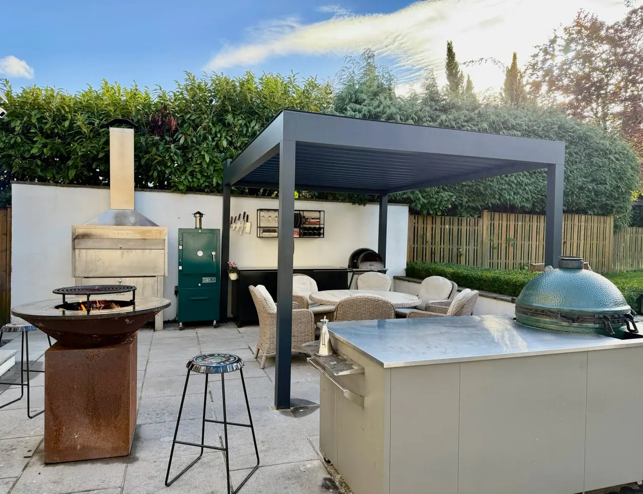 Modern outdoor entertaining space with multiple cooking stations, seating areas, and fire pits in a landscaped garden.