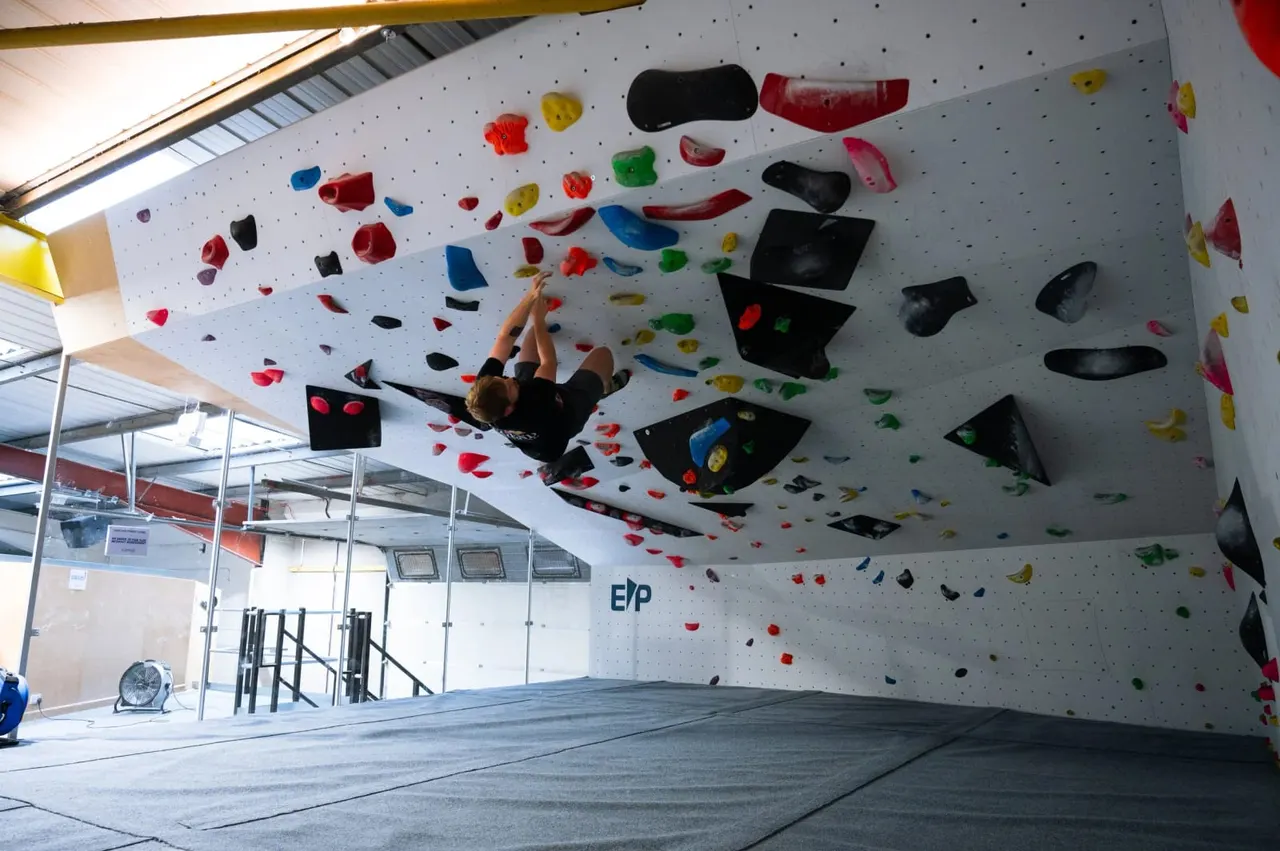 A person indoor rock climbing on a large overhanging white wall with colourful handholds.