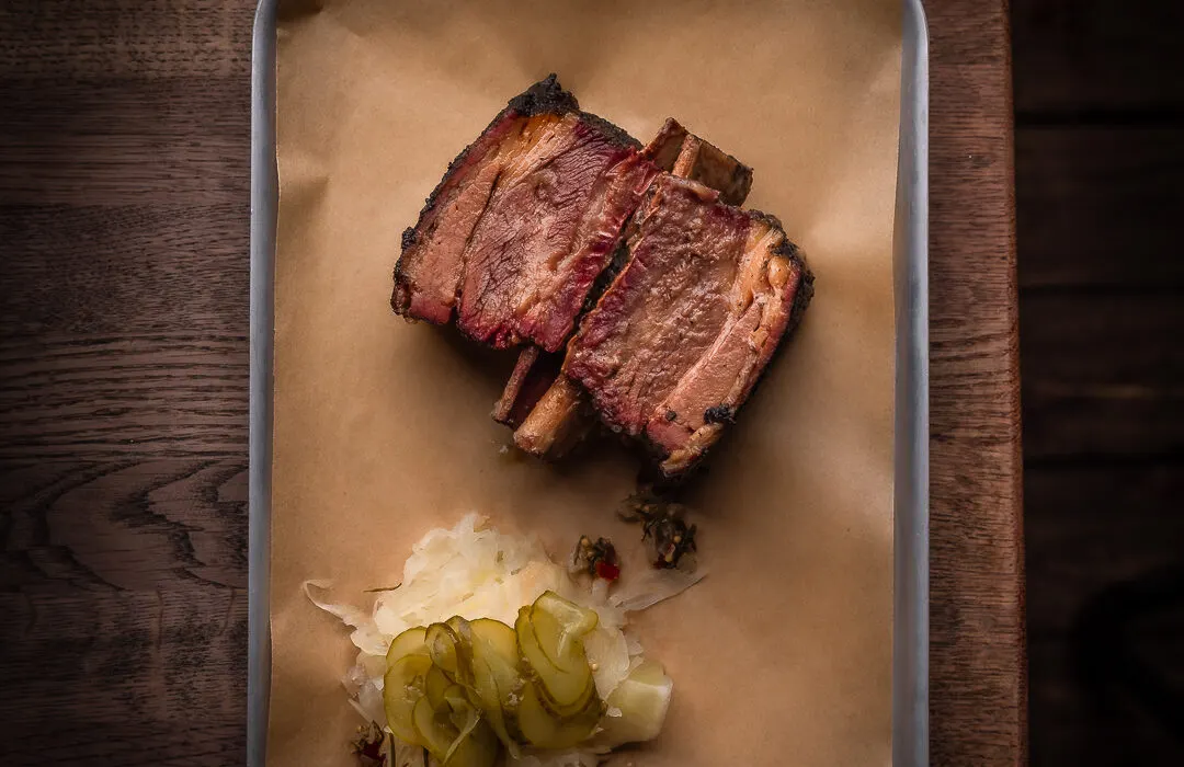 Sliced medium-rare steak with charred edges served on parchment paper with pickled vegetables.