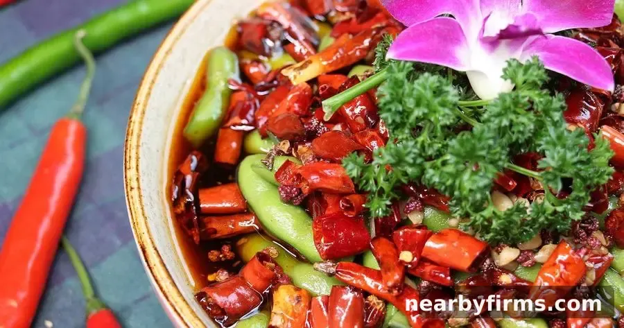 Spicy stir-fried dish with red peppers, green vegetables and fresh herbs in a bowl, garnished with pink flower.