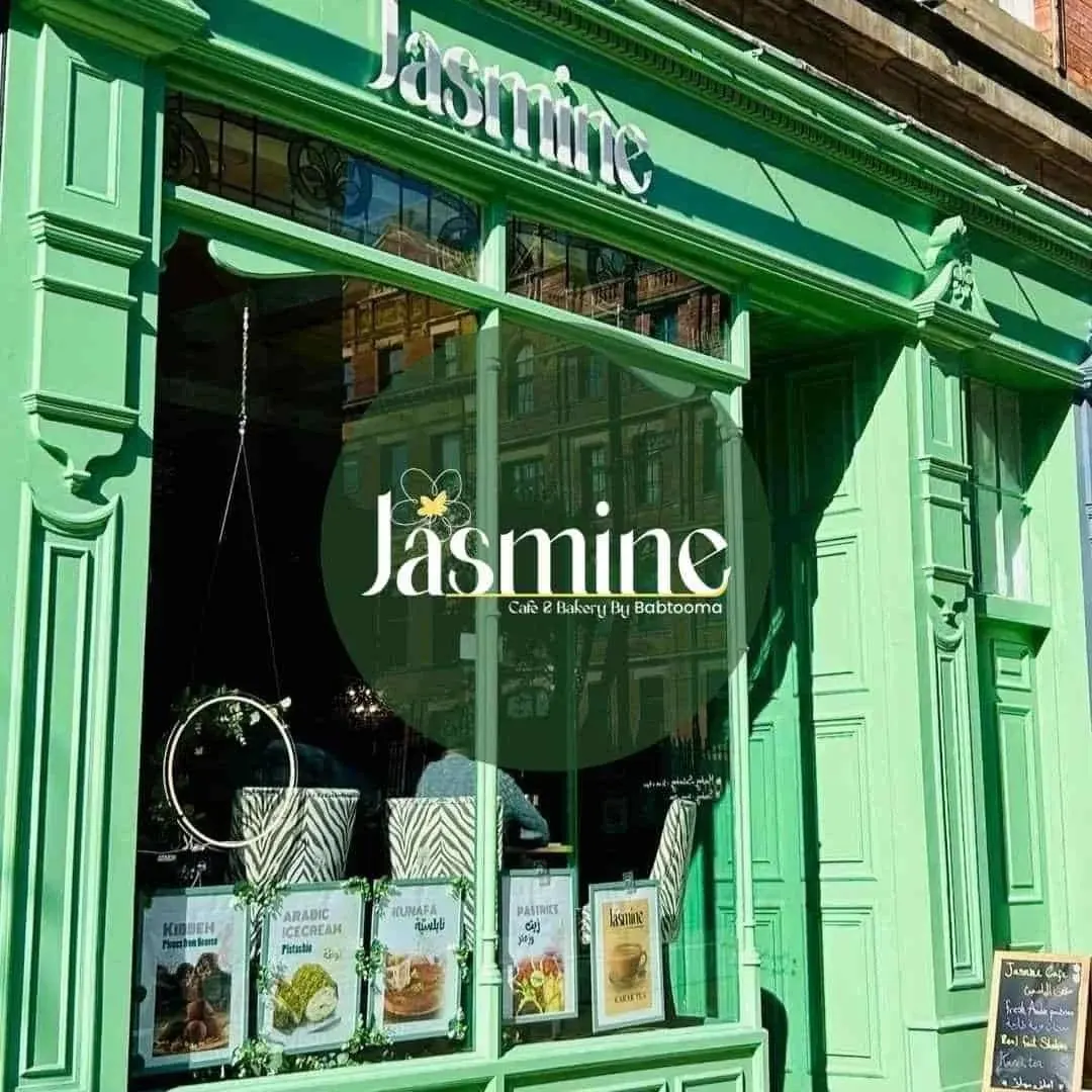 Bright green storefront of a café and bakery with large windows displaying menu boards and hanging plants.