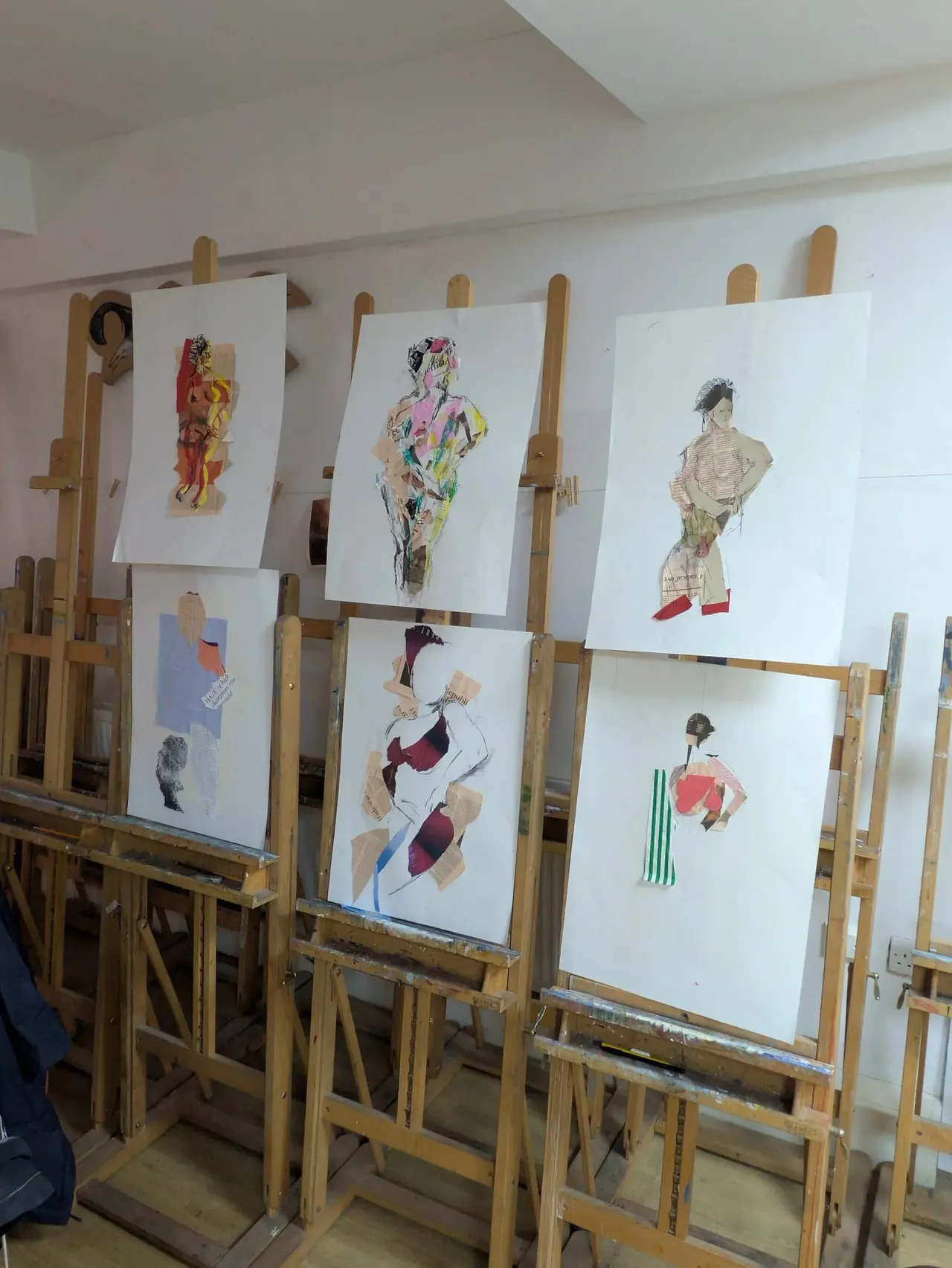 Multiple life drawing sketches of figures pinned to wooden easels in an art studio.