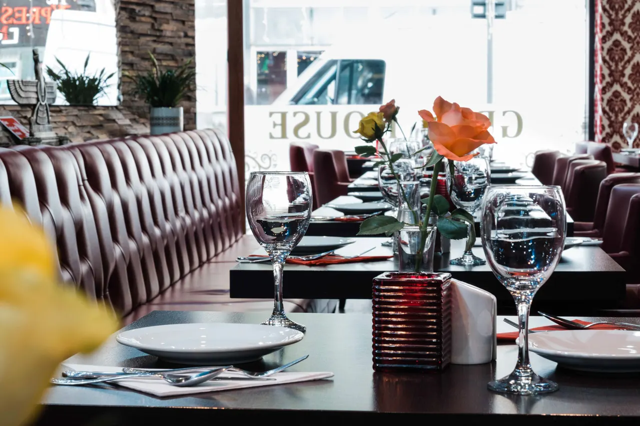 Formal dining table set with place settings, wine glasses, cutlery and orange roses in a restaurant with burgundy seating.