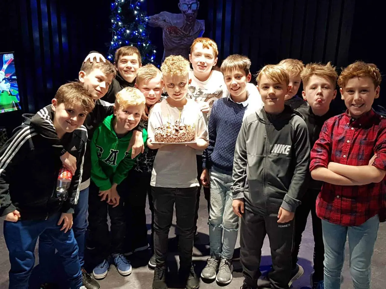 Group of young children posing indoors with popcorn, decorated Christmas tree and skull prop visible behind them.