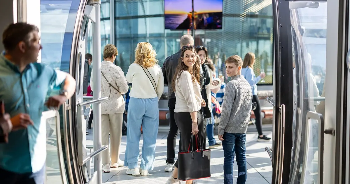 Visitors enjoying a bright, modern observation tower interior with panoramic windows overlooking a coastal cityscape.