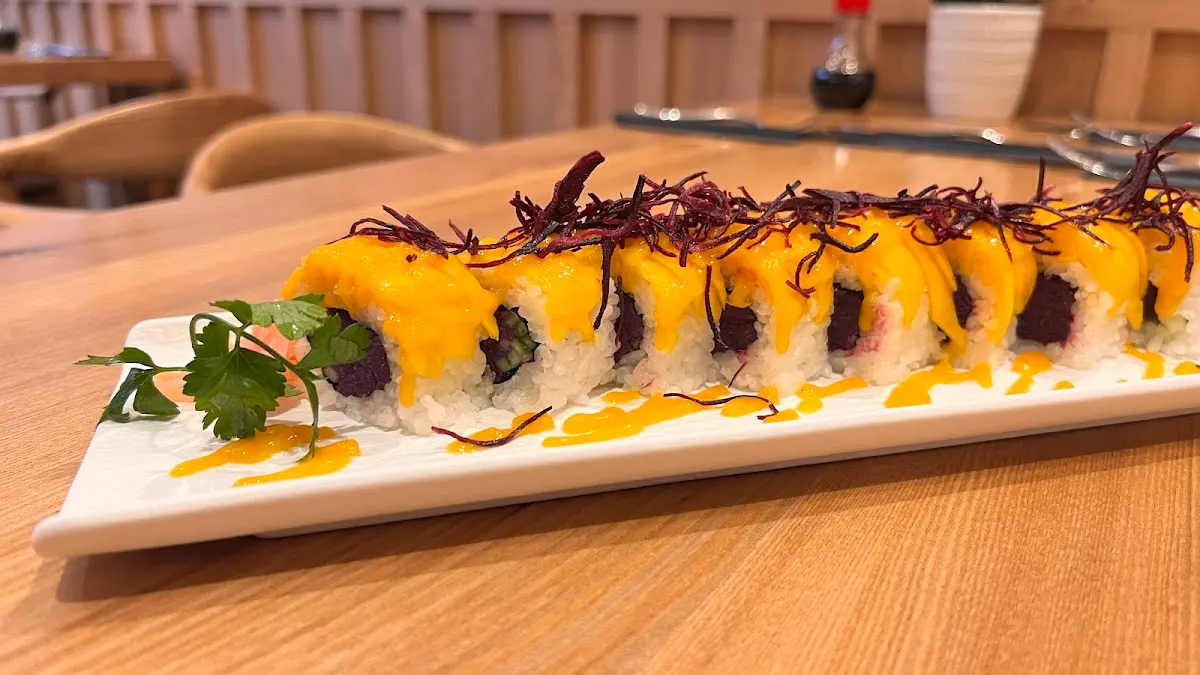 Sushi roll topped with yellow sauce and beetroot garnish on a white plate in a dining room.