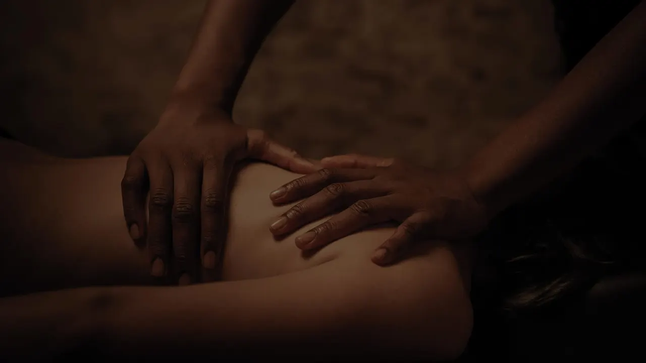 Hands performing a massage on a client's back in warm, dimly lit spa setting.