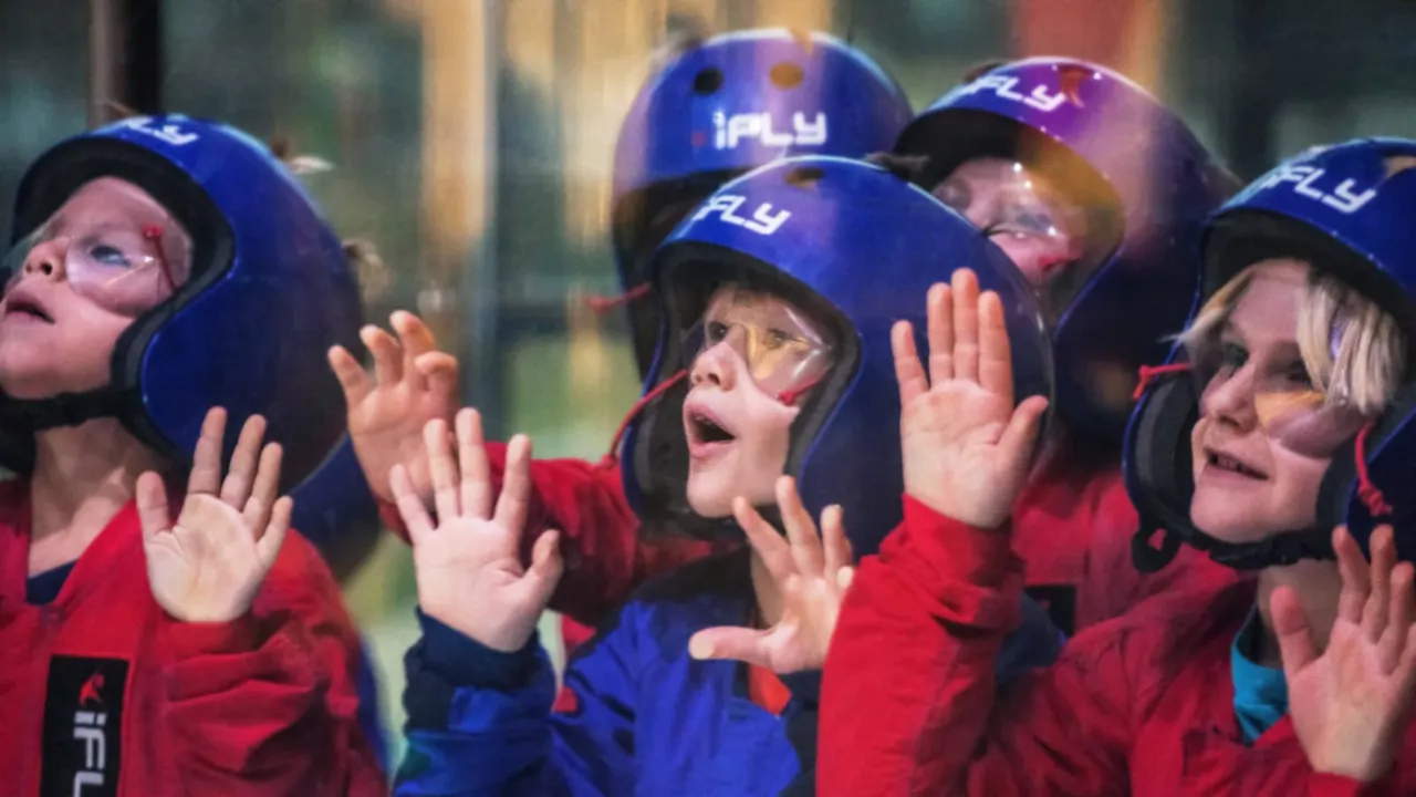 Children wearing protective helmets and jumpsuits experience indoor skydiving in a wind tunnel.