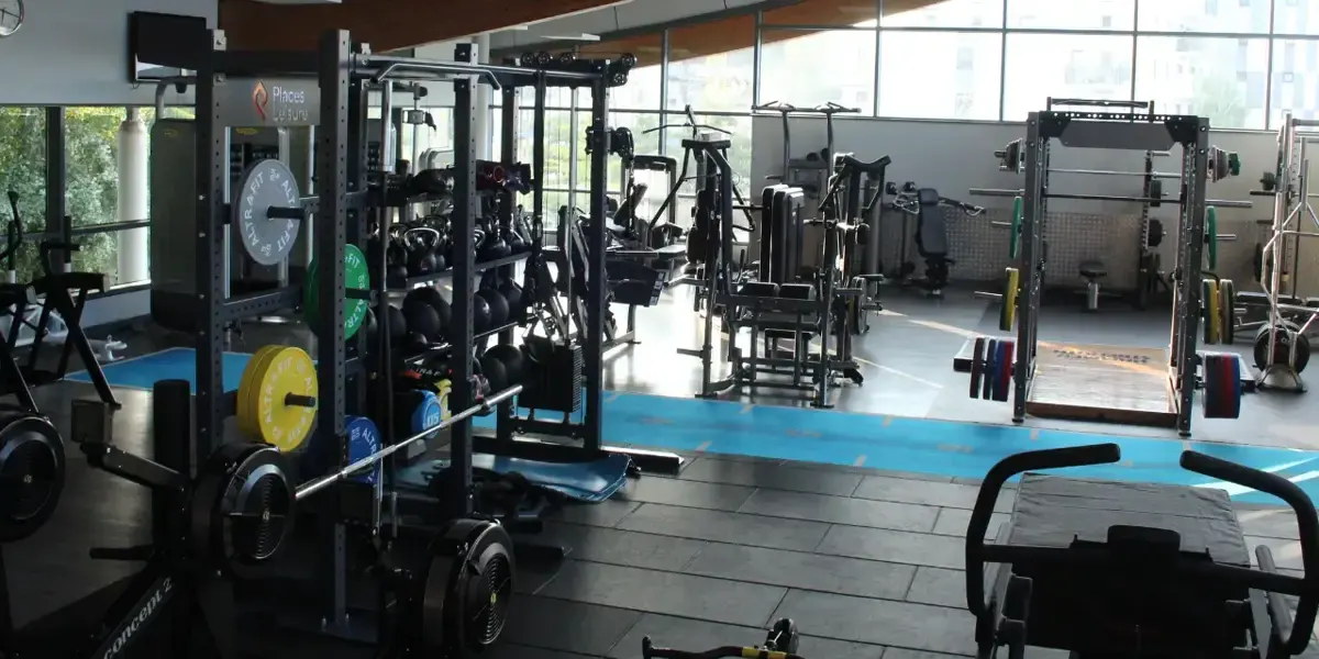 Bright gym interior with various exercise machines, weights, stationary bikes and free weights scattered throughout the spacious facility with large windows.