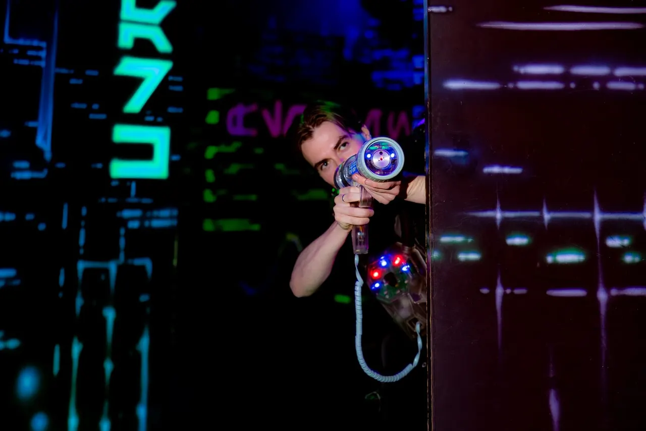 Person aiming a glowing laser gun during an indoor laser tag game in a darkened arena.